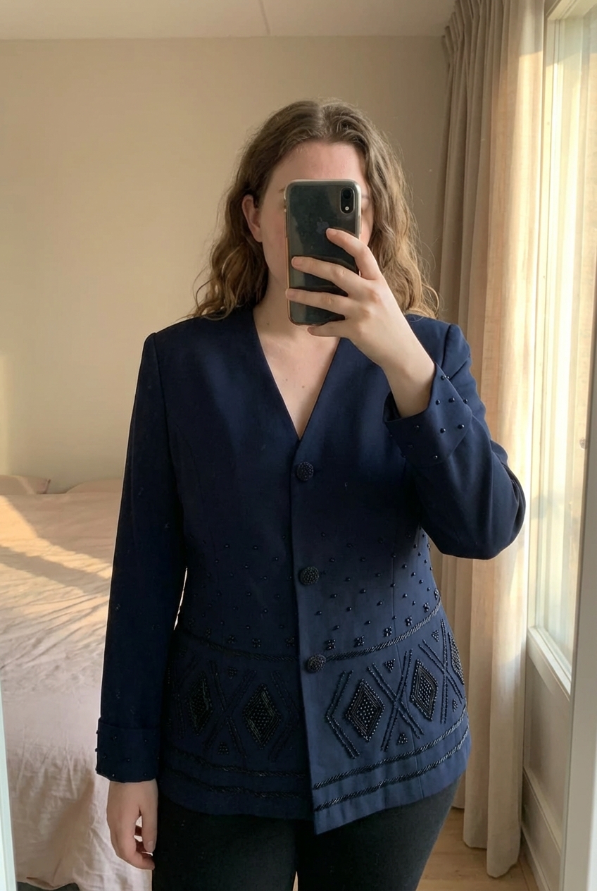 Une personne en Blazer / veste femme debout, face à la caméra, avec une silhouette légèrement plus ronde, dans une chambre à la lumière douce, avec une lumière naturelle filtrant par la fenêtre.