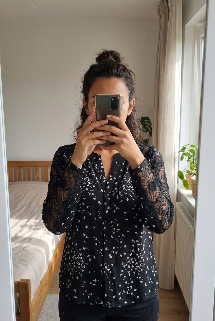 Une personne en Chemise 123 noir et dentelle excellent état debout, face à la caméra, dans une chambre à la lumière douce, avec une lumière naturelle filtrant par la fenêtre.