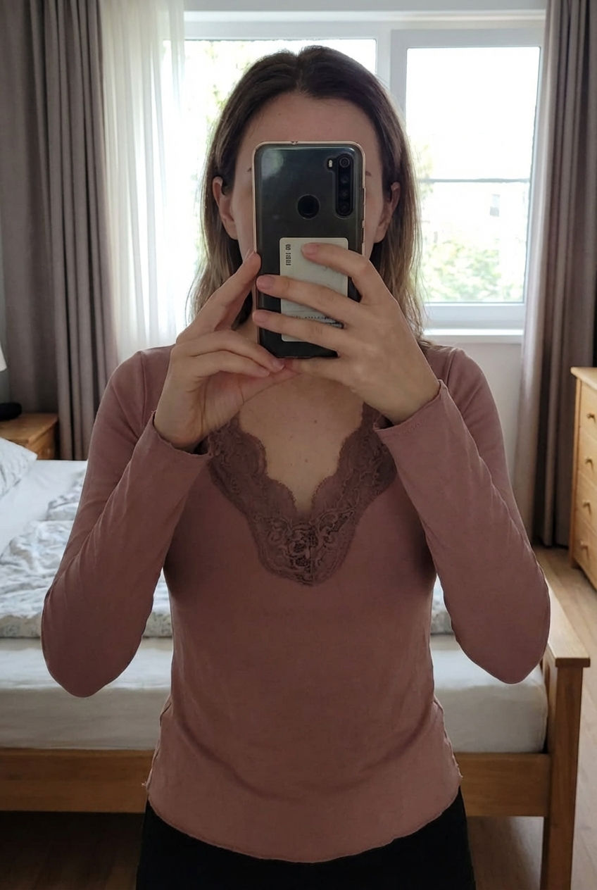 Top dentelle debout, face à la caméra, dans une chambre à la lumière douce, avec une lumière naturelle filtrant par la fenêtre.