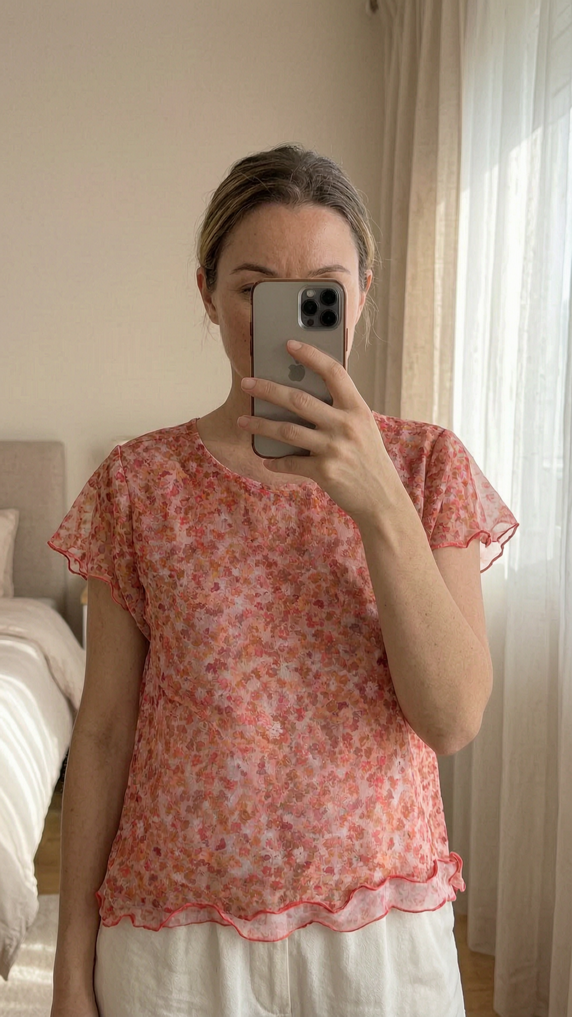 Summer short top orange flowers Anthropologie size m debout, face à la caméra, dans une chambre à la lumière douce, avec une lumière naturelle filtrant par la fenêtre.