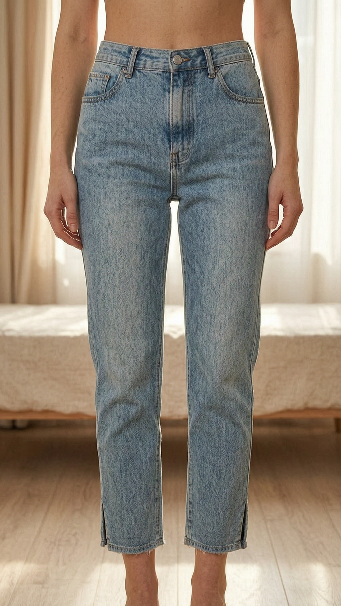 Jeans taille haute bleu clair à fente debout, face à la caméra, dans une chambre à la lumière douce, avec une lumière naturelle filtrant par la fenêtre.