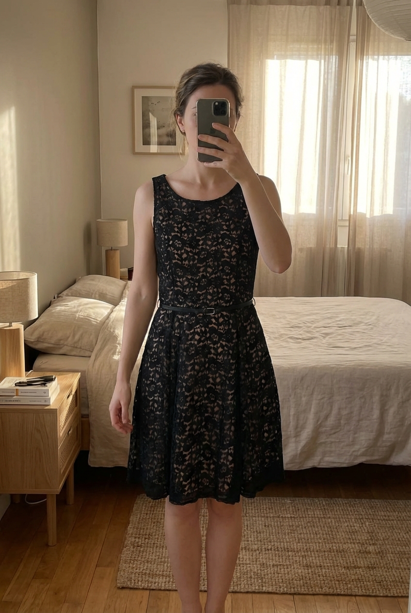 Robe en dentelle noire doublée nude – Cache Cache debout, face à la caméra, dans une chambre à la lumière douce, avec une lumière naturelle filtrant par la fenêtre.