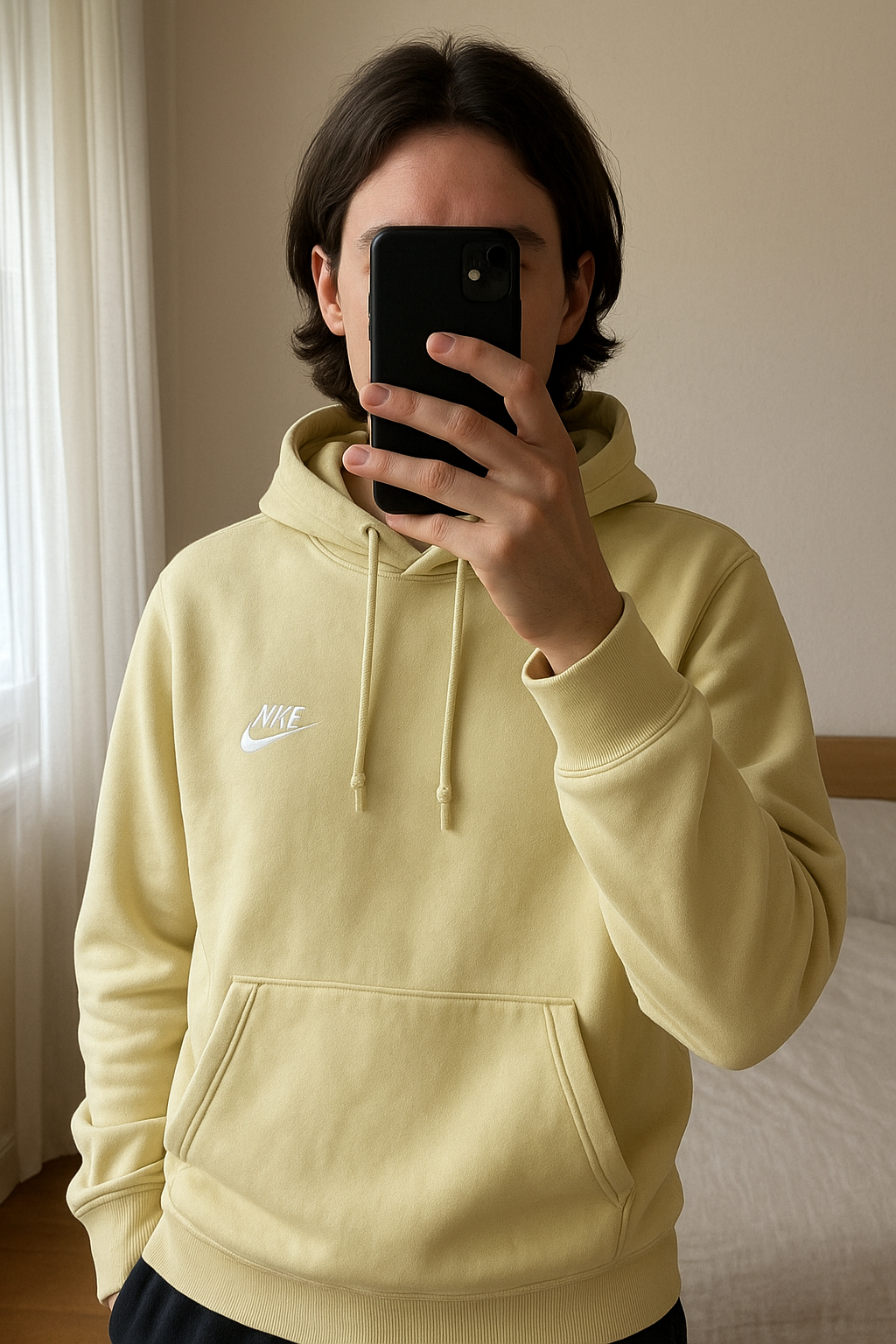 Nike pull debout, face à la caméra, dans une chambre à la lumière douce, avec une lumière naturelle filtrant par la fenêtre.