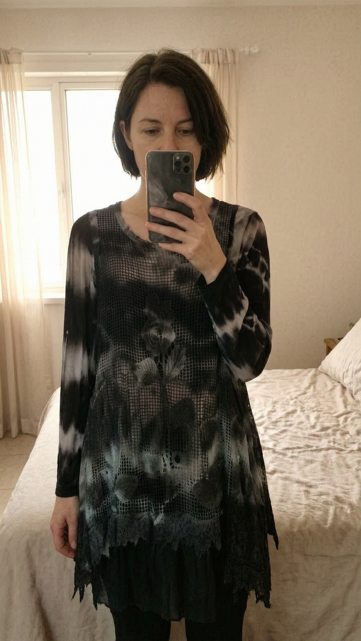 Tunique dentelle debout, face à la caméra, dans une chambre à la lumière douce, avec une lumière naturelle filtrant par la fenêtre.