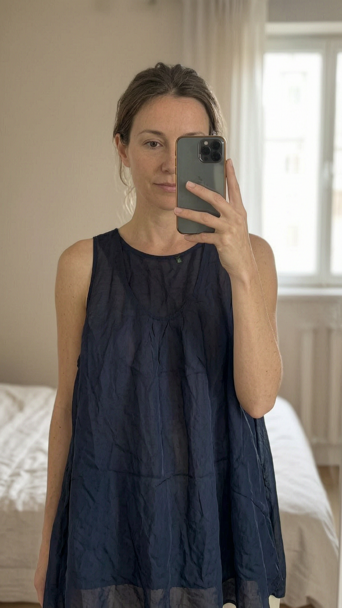 Haut fluide Benetton L - Maglietta canotte Benetton donna in piedi, rivolto verso la fotocamera, in una camera da letto con luce soffusa e luce naturale che filtra dalla finestra.