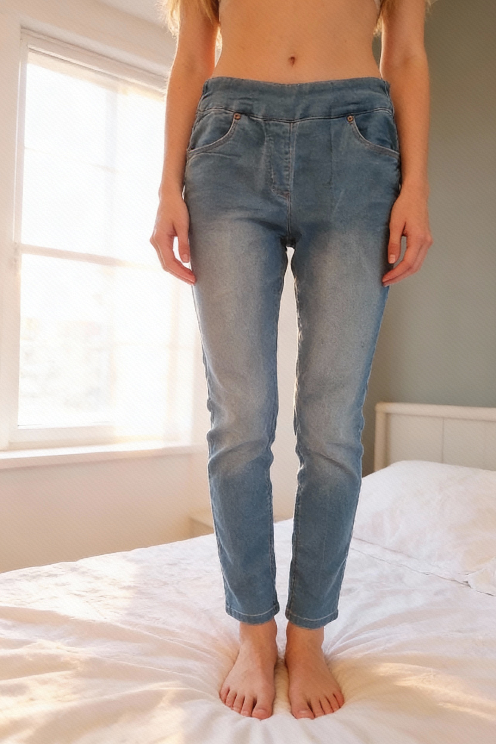 Jegging neuf debout, face à la caméra, dans une chambre à la lumière douce, avec une lumière naturelle filtrant par la fenêtre.