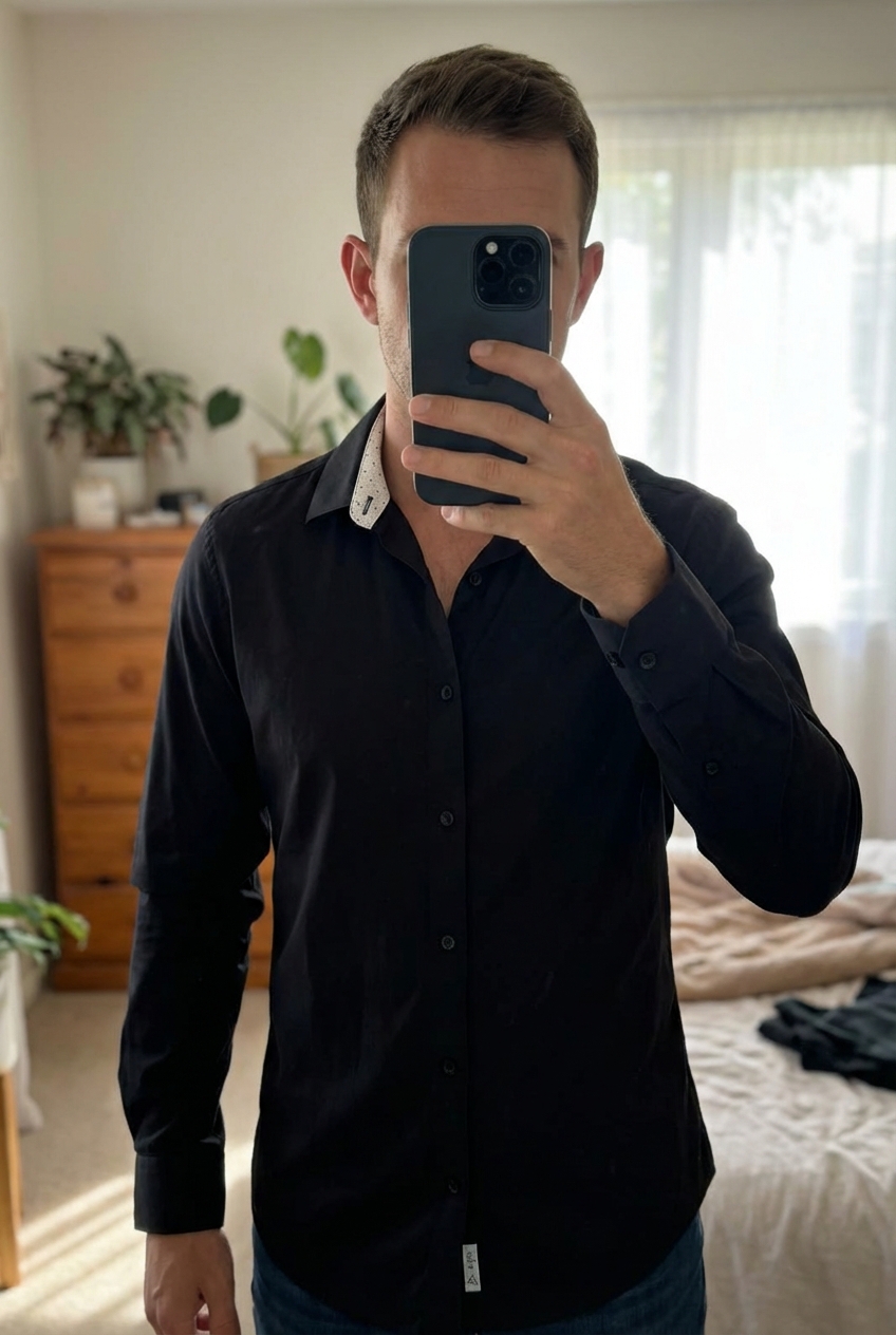 Une personne en 🖤 Jules chemise noire slim fit debout, face à la caméra, dans une chambre à la lumière douce, avec une lumière naturelle filtrant par la fenêtre.