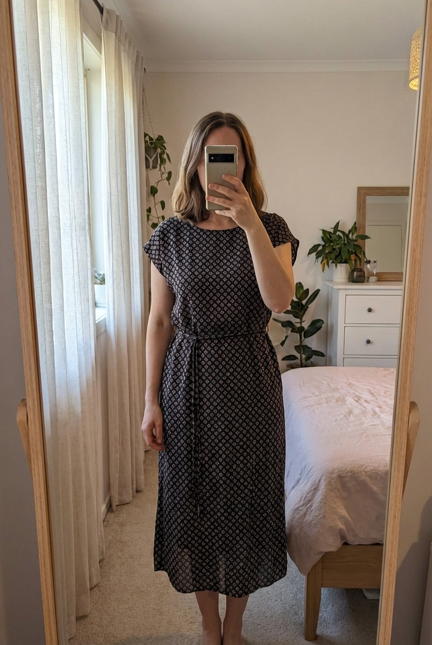 Kleid mit tollem Muster | Gr. 32-34 aufrecht stehend, der Kamera zugewandt, in einem sanft beleuchteten Schlafzimmer, mit natürlichem Licht, das durch ein Fenster fällt.