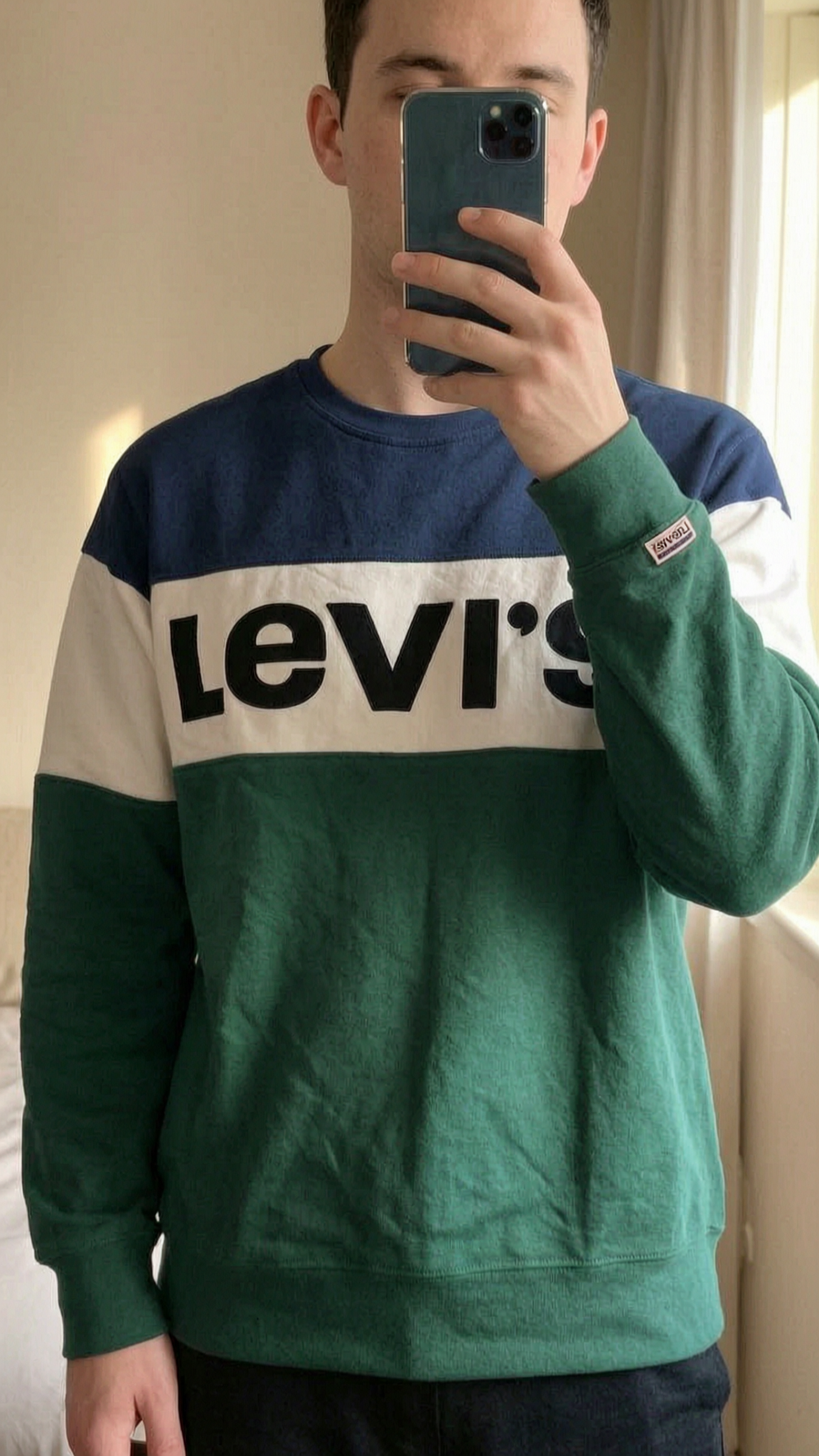 Levi's Pullover aufrecht stehend, der Kamera zugewandt, in einem sanft beleuchteten Schlafzimmer, mit natürlichem Licht, das durch ein Fenster fällt.