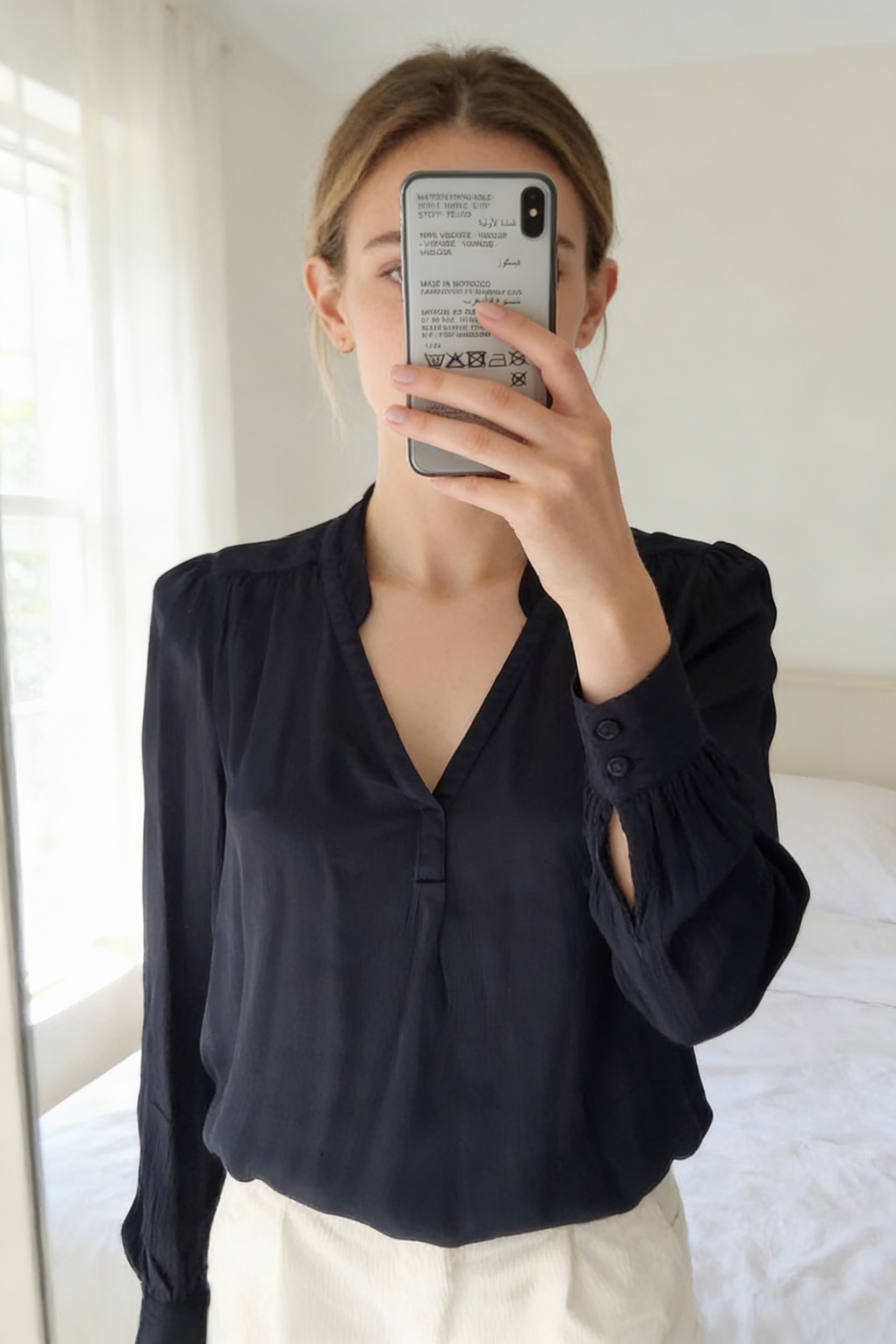 Blouse Maison 123 debout, face à la caméra, dans une chambre à la lumière douce, avec une lumière naturelle filtrant par la fenêtre.