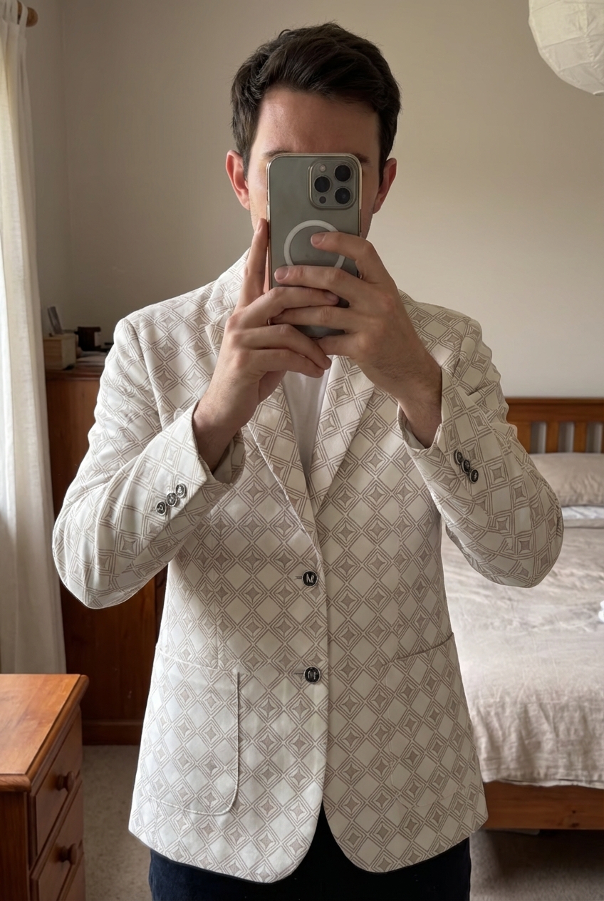 Costume homme blanc creme à motif etoilé debout, face à la caméra, dans une chambre à la lumière douce, avec une lumière naturelle filtrant par la fenêtre.