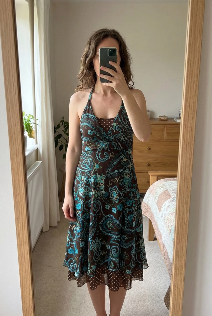 Robe marron bleu et vert alex(e) debout, face à la caméra, dans une chambre à la lumière douce, avec une lumière naturelle filtrant par la fenêtre.