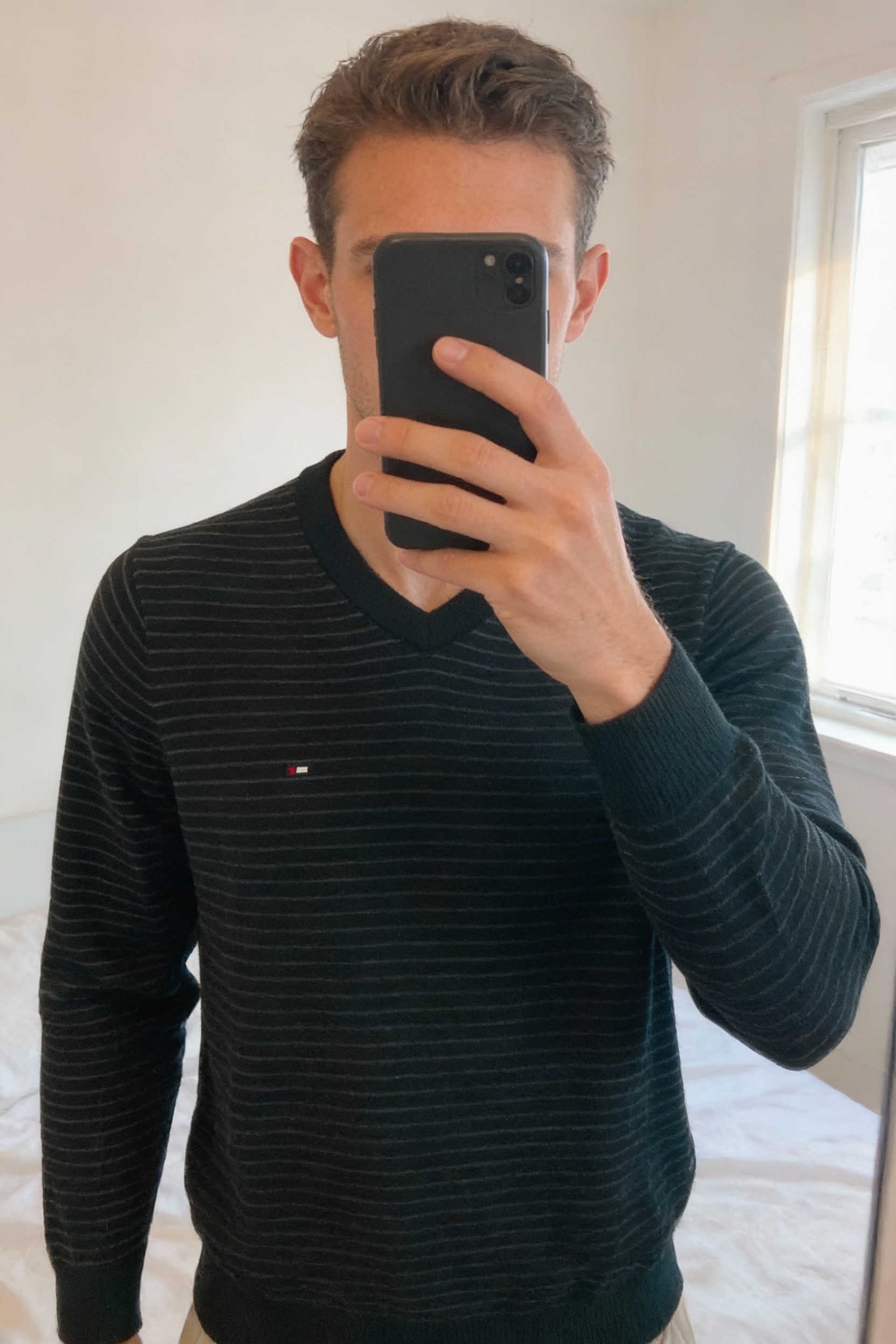 Tommy Hilfiger - Pull - Taille M debout, face à la caméra, dans une chambre à la lumière douce, avec une lumière naturelle filtrant par la fenêtre.