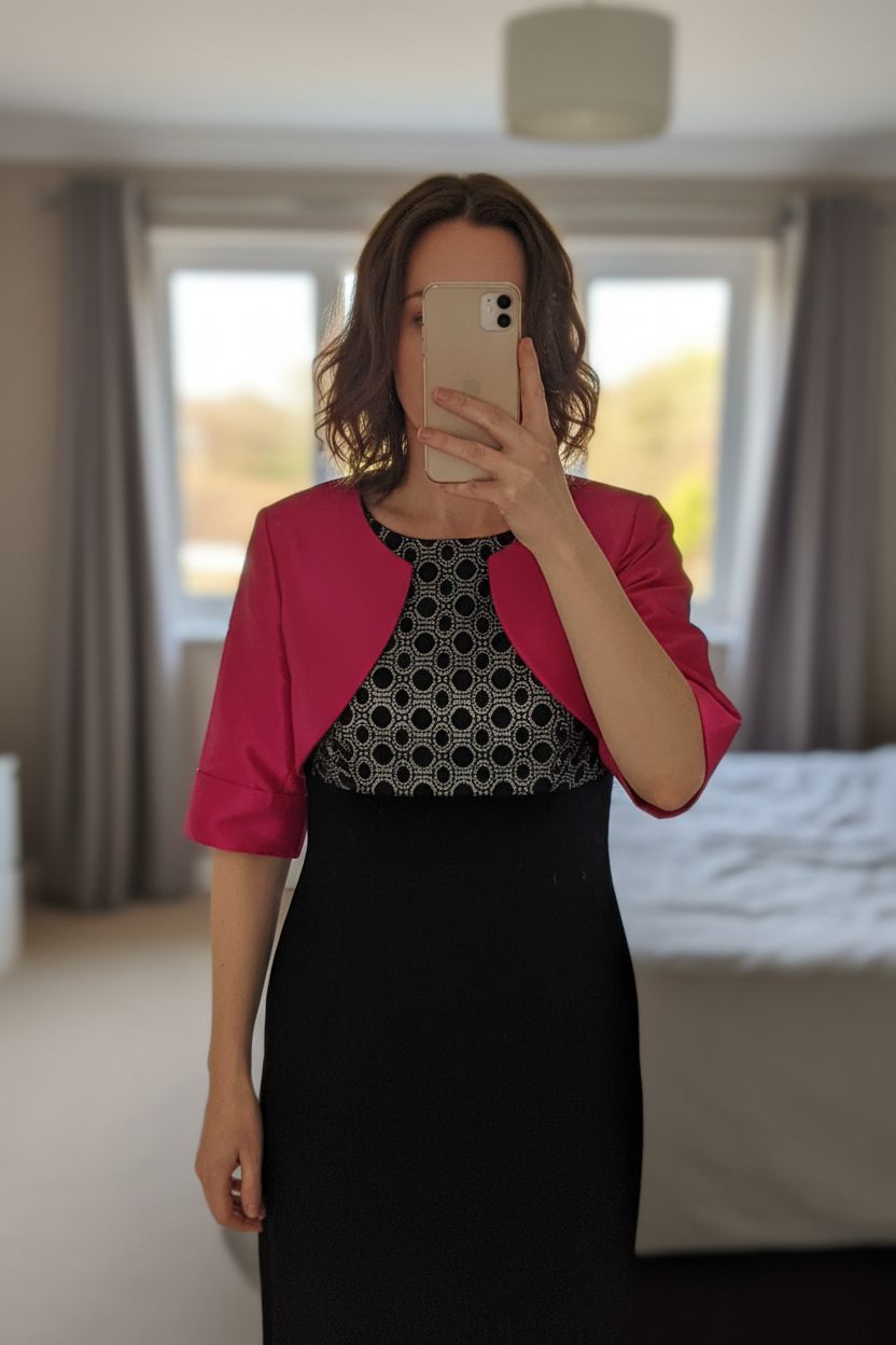Silver and black dress with fuschia pink Bolero standing straight facing the camera, in a softly lit bedroom setting, with gentle natural light filtering through a window.