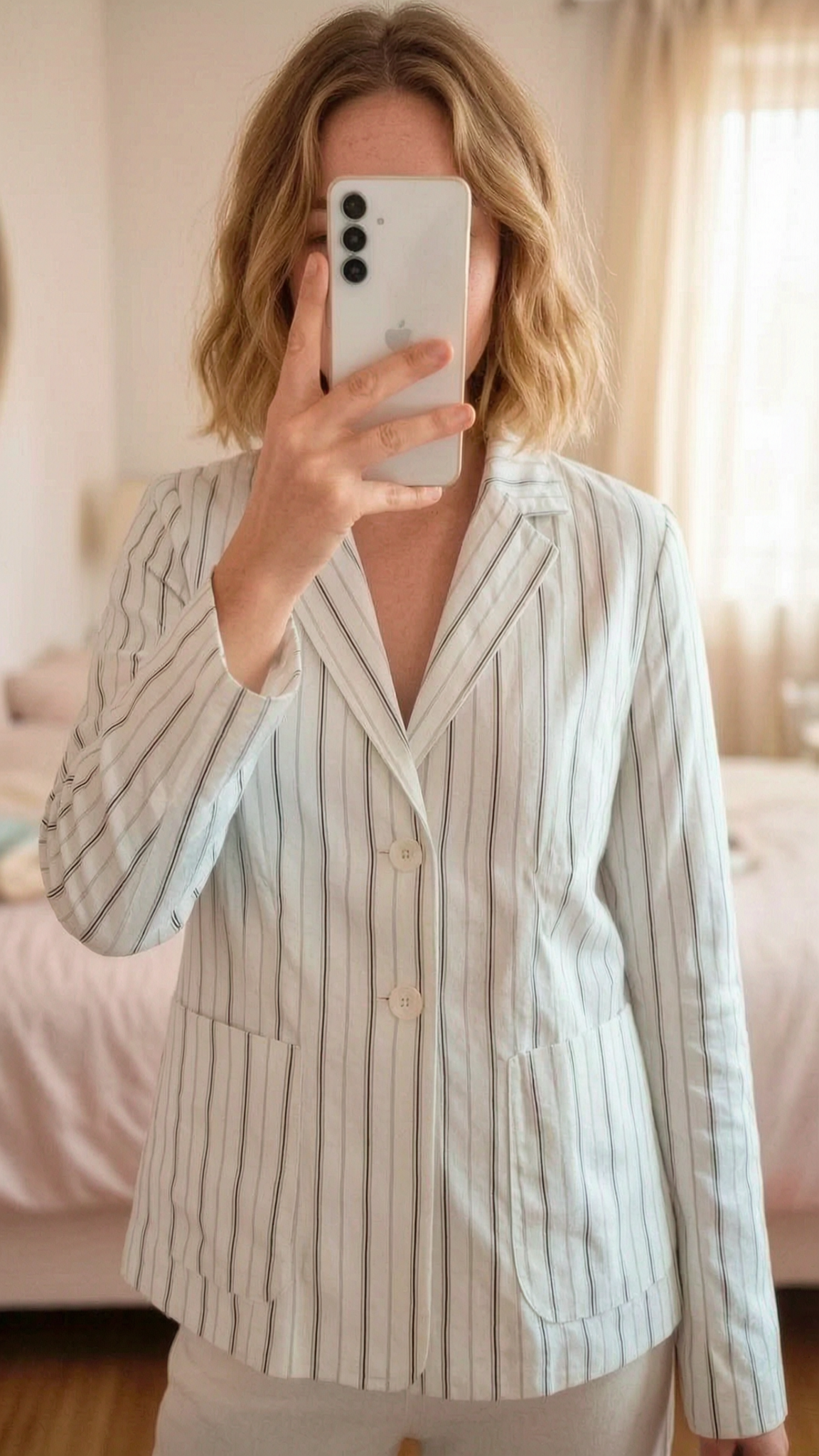 Blazer branco com riscas pretas para mulher, algodão, veste 40. Marca Agá. em pé, de frente para a câmera, em um quarto com iluminação suave e luz natural filtrando pela janela.