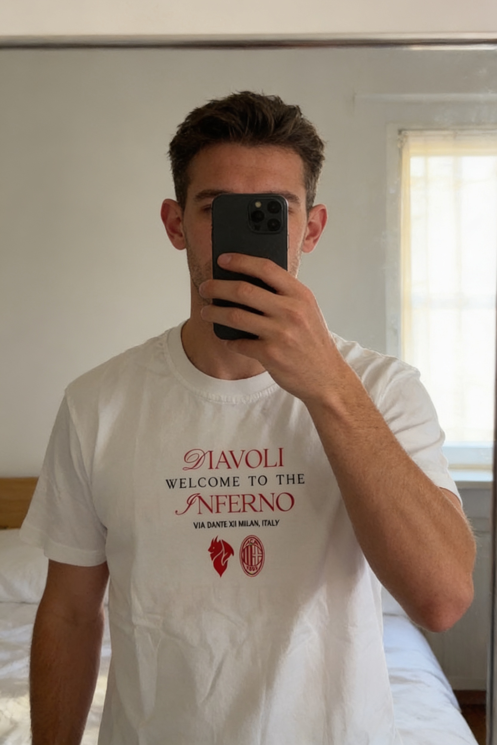 Teeshirt AC Milan homme S debout, face à la caméra, dans une chambre à la lumière douce, avec une lumière naturelle filtrant par la fenêtre.