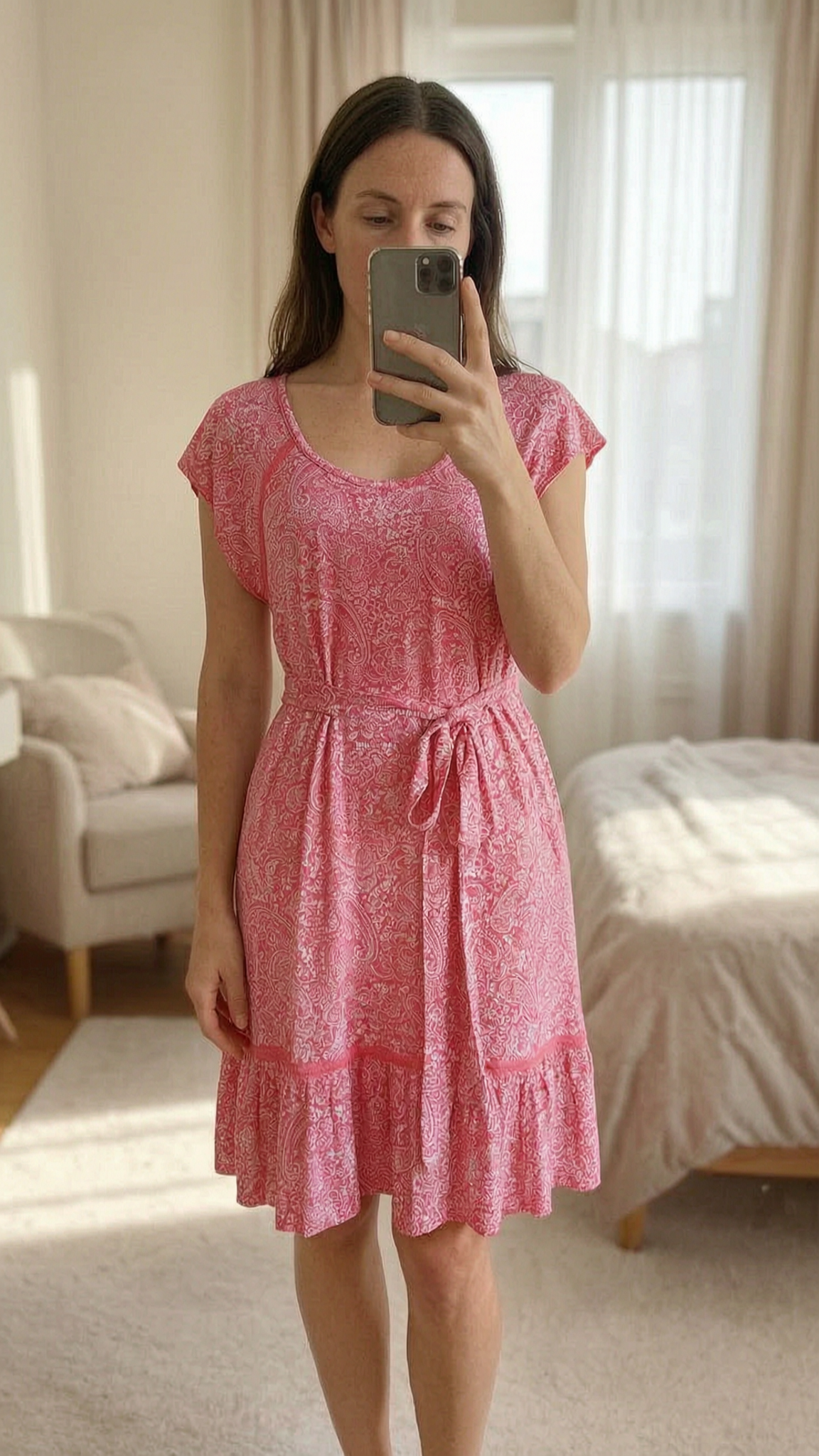Vestido estampado talla M / Robe rose imprimé de pie, mirando a la cámara, en un dormitorio con luz suave y natural filtrándose por la ventana.