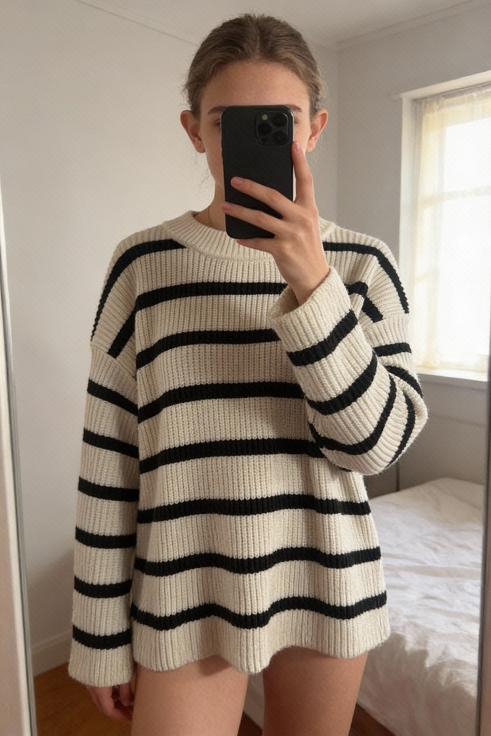 Una persona in Pull hiver loose H&M S - Maglione inverno H&M in piedi, rivolto verso la fotocamera, in una camera da letto con luce soffusa e luce naturale che filtra dalla finestra.