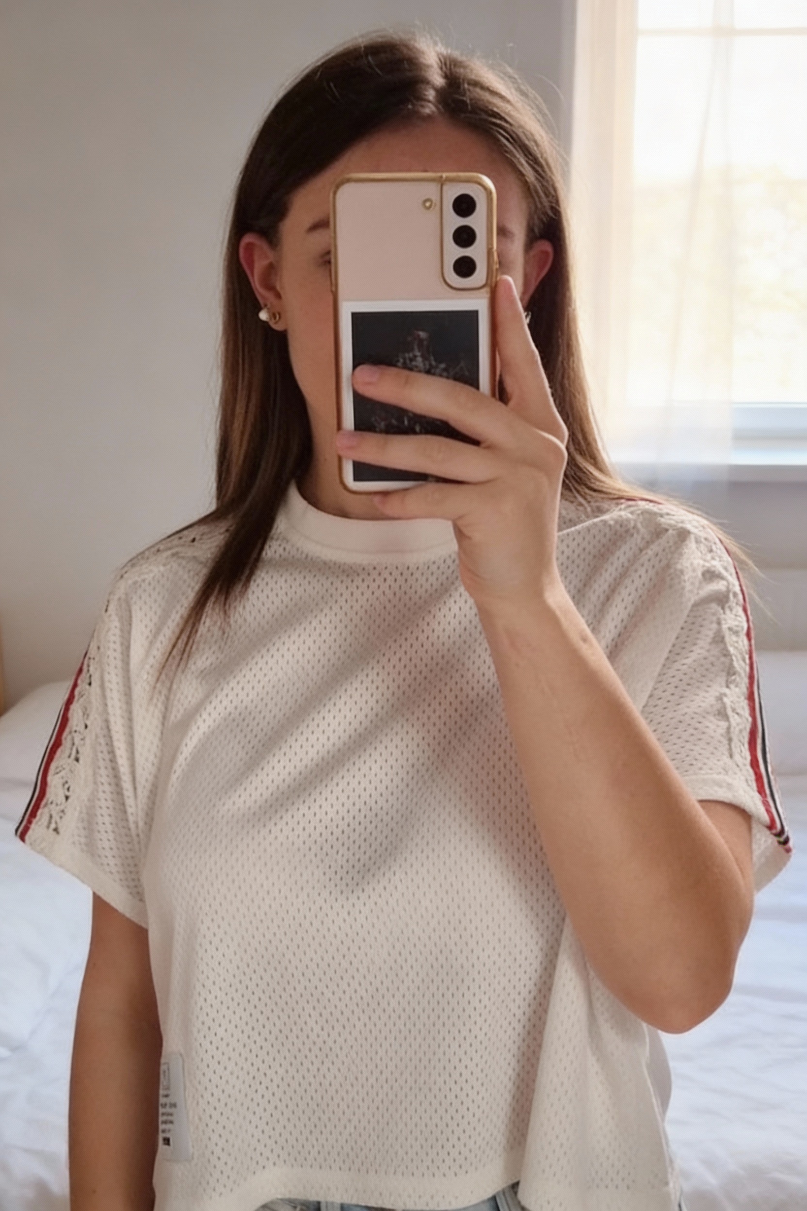 T-shirt The Kooples debout, face à la caméra, dans une chambre à la lumière douce, avec une lumière naturelle filtrant par la fenêtre.