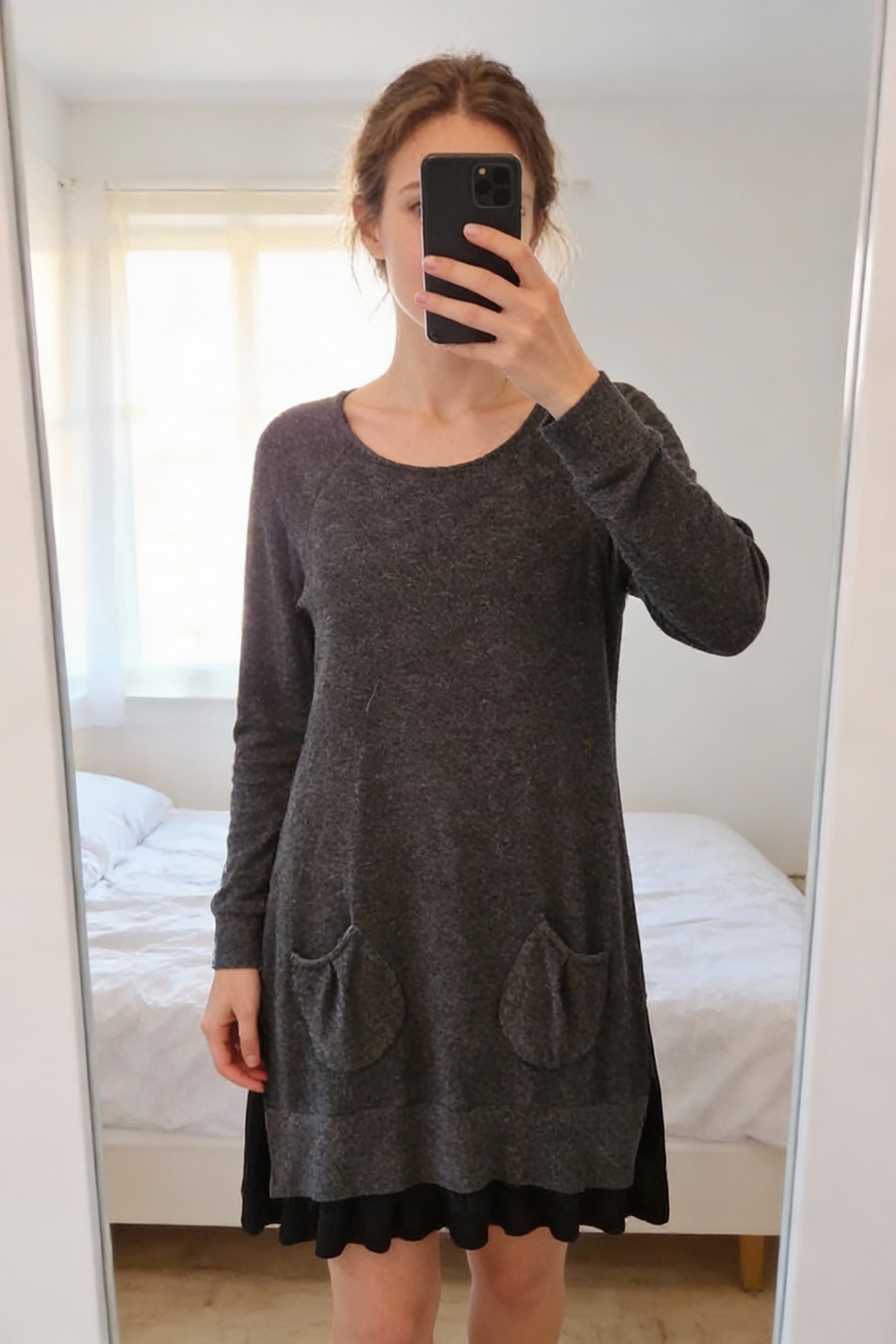 Robe grise agréable au toucher debout, face à la caméra, dans une chambre à la lumière douce, avec une lumière naturelle filtrant par la fenêtre.