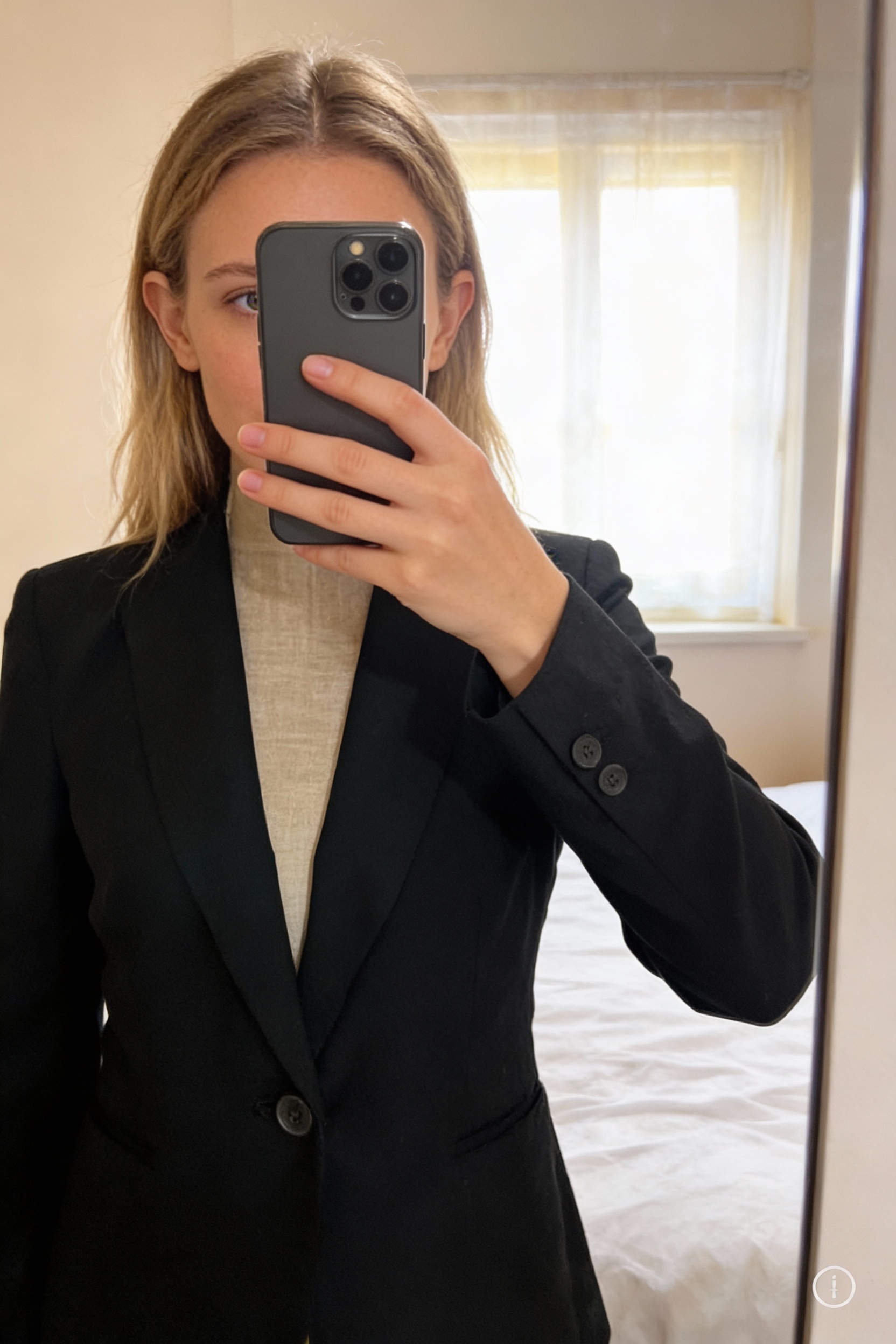Blazer Zara noir taille S debout, face à la caméra, dans une chambre à la lumière douce, avec une lumière naturelle filtrant par la fenêtre.