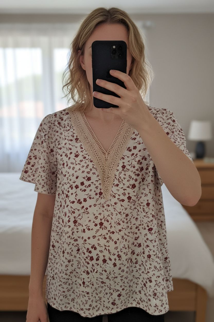 Bouse manches courtes col V taille M debout, face à la caméra, dans une chambre à la lumière douce, avec une lumière naturelle filtrant par la fenêtre.