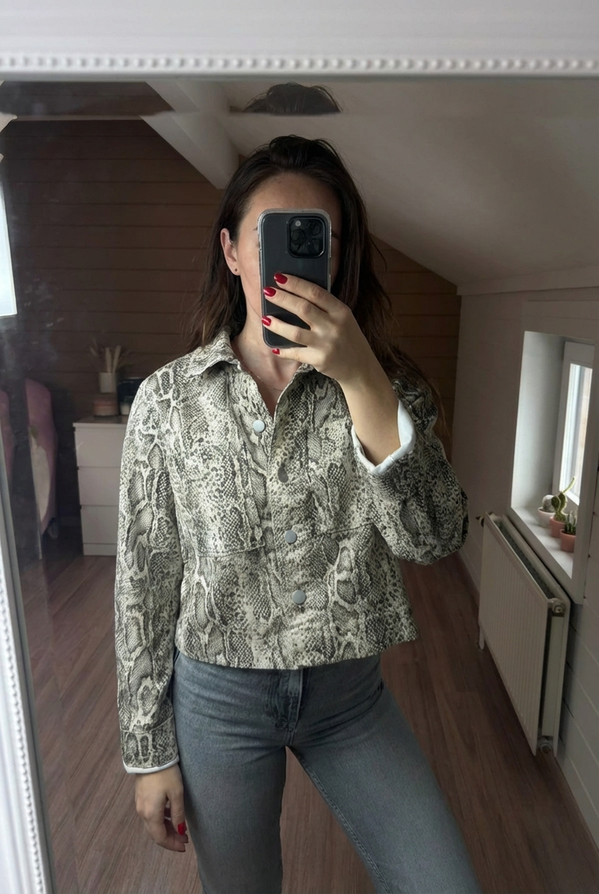 Veste vila beige noir gris en python courte surchemise bouton col droit animal debout, face à la caméra, dans une chambre à la lumière douce, avec une lumière naturelle filtrant par la fenêtre.