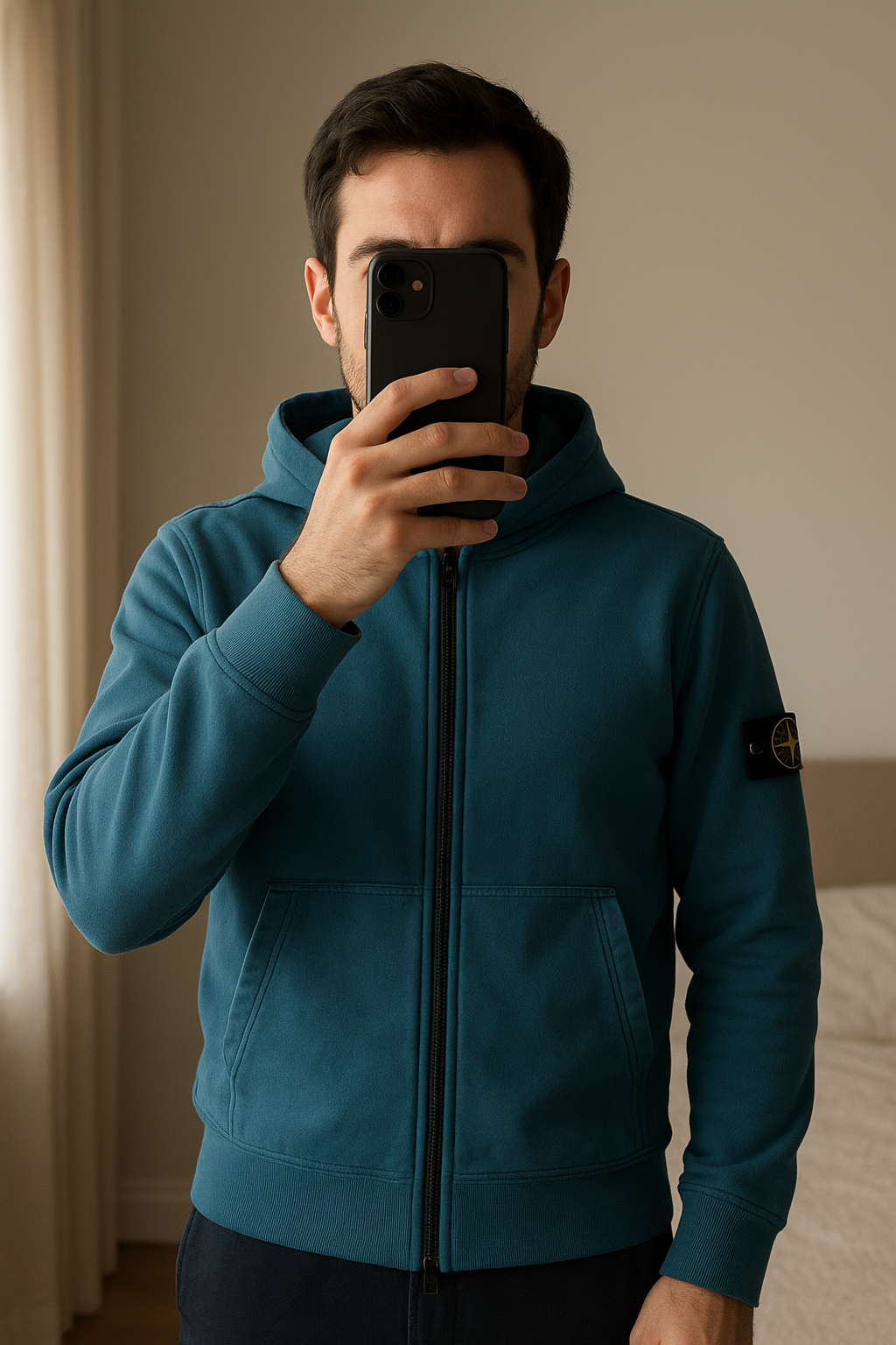 Veste stone island debout, face à la caméra, dans une chambre à la lumière douce, avec une lumière naturelle filtrant par la fenêtre.
