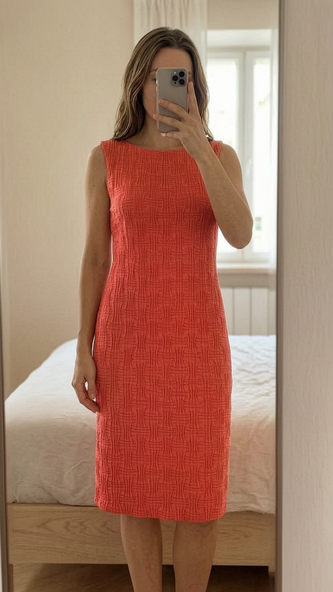 Beautiful midi coral dress with 3D pattern em pé, de frente para a câmera, em um quarto com iluminação suave e luz natural filtrando pela janela.