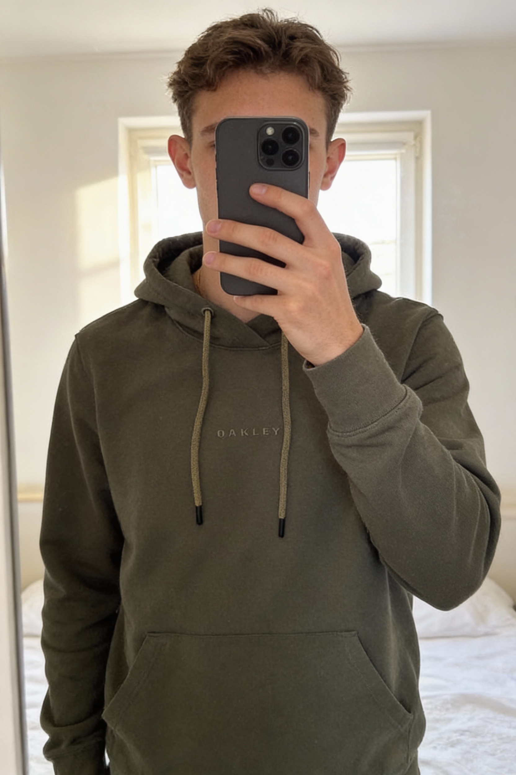 pull oakley debout, face à la caméra, dans une chambre à la lumière douce, avec une lumière naturelle filtrant par la fenêtre.