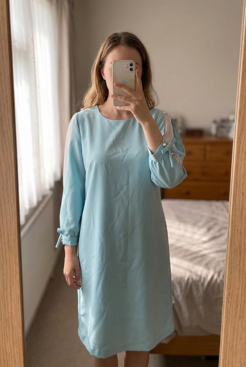 Una persona con Vestido azul claro con manga semi transparente de pie, mirando a la cámara, en un dormitorio con luz suave y natural filtrándose por la ventana.