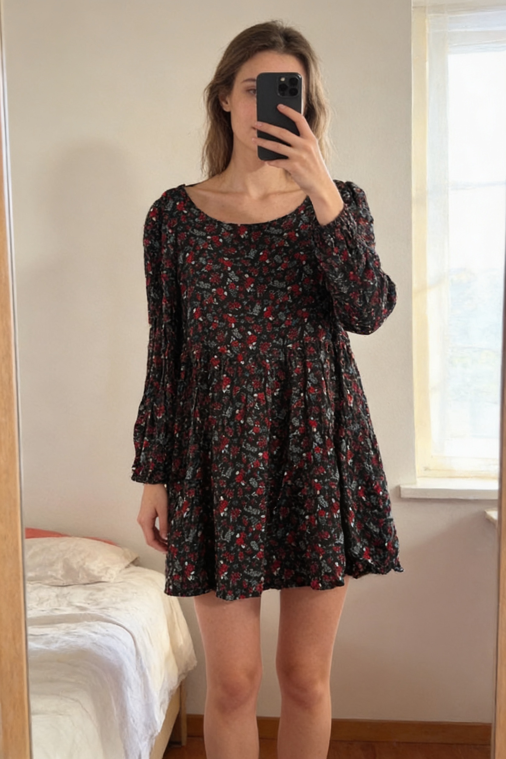 Robe femme à motifs M - Abito Ovs donna M in piedi, rivolto verso la fotocamera, in una camera da letto con luce soffusa e luce naturale che filtra dalla finestra.