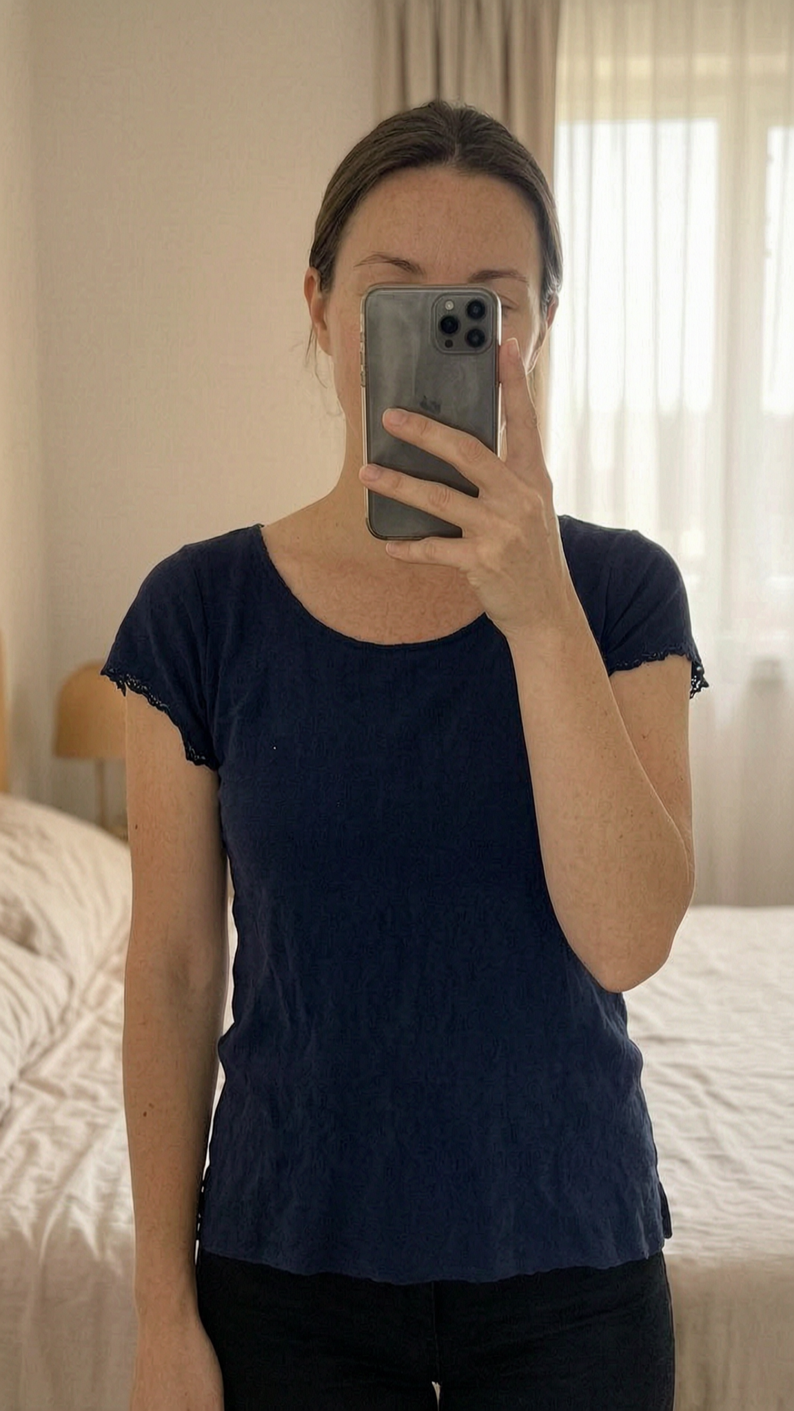 T-shirt tally Weijl bleu marine dentelle debout, face à la caméra, dans une chambre à la lumière douce, avec une lumière naturelle filtrant par la fenêtre.