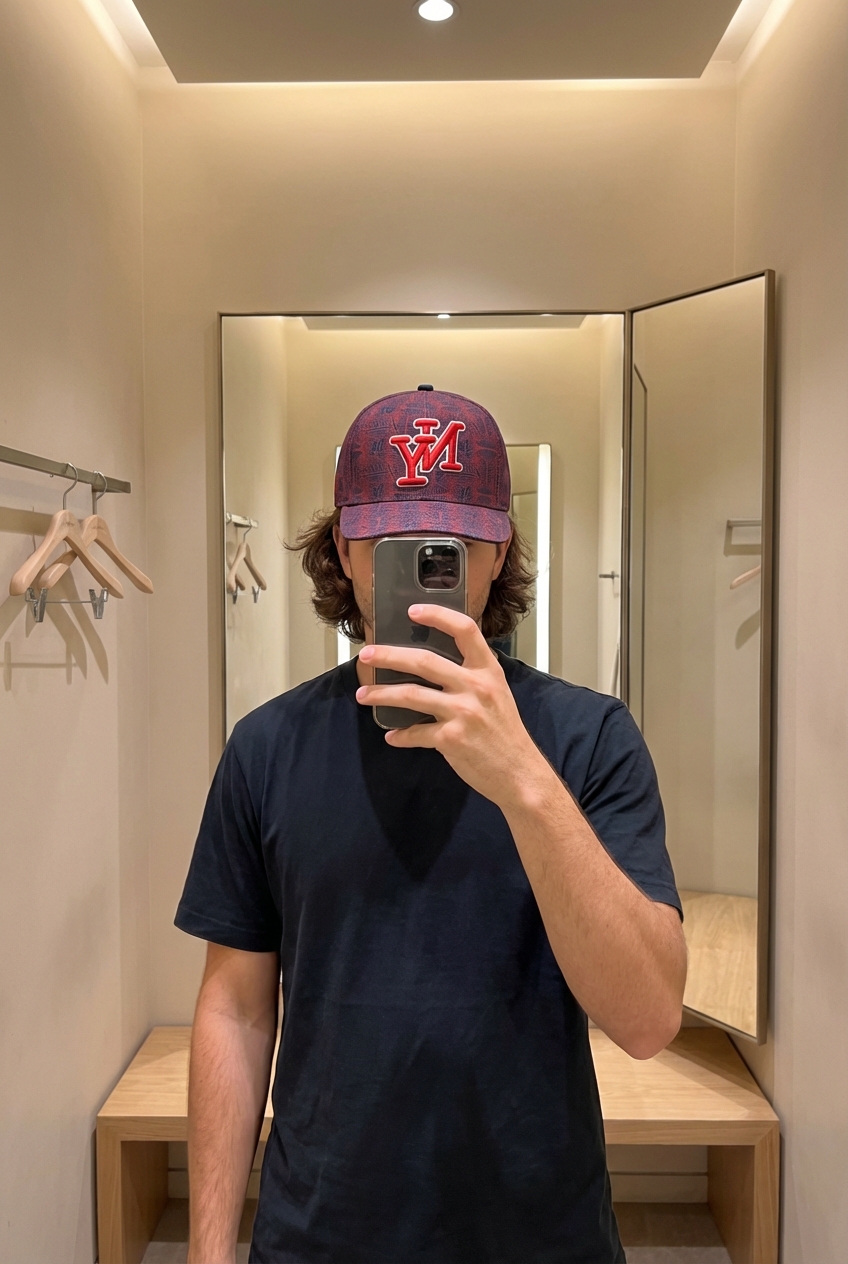 Una persona in Cappellino snapback NY – fantasia all over in piedi, rivolto verso la fotocamera, in un camerino in stile boutique con specchio e decorazioni neutre.