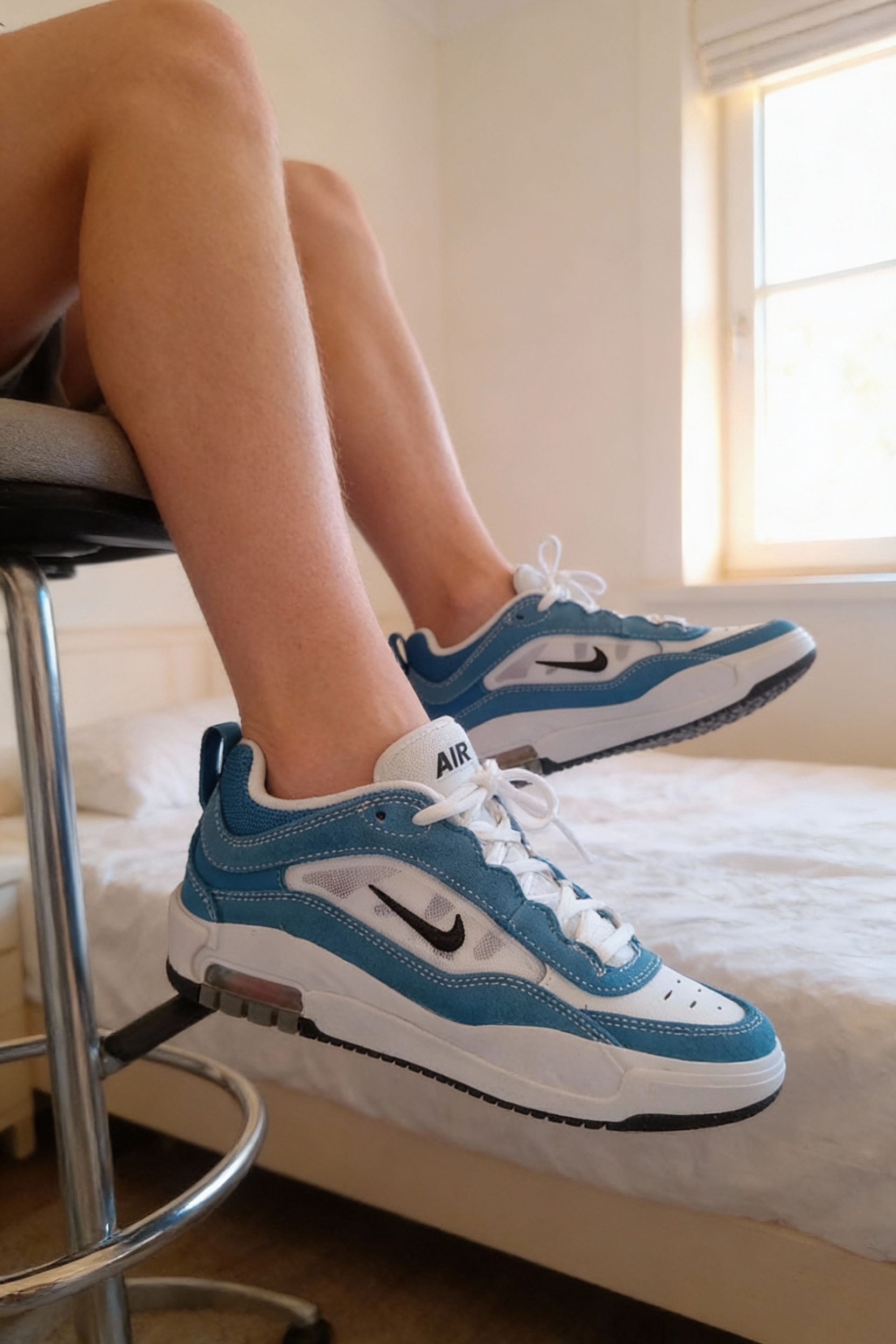 Una persona con Nike Air Max Ishod Star azul/negro/blanco – talla 38 sentado en una silla alta, con postura relajada, con tipo de cuerpo delgado, en un dormitorio con luz suave y natural filtrándose por la ventana.